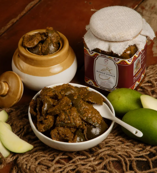 Homemade mango pickle in a ceramic jar with spices on the side.